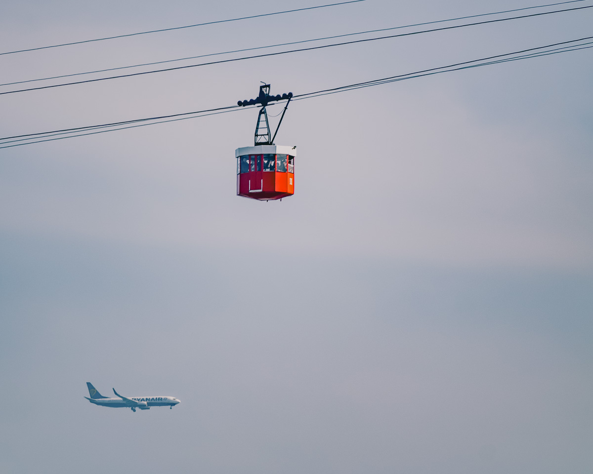 A view of Barcelona’s large cable car with an airplane in the background, taken from above Montjuïc Castle.