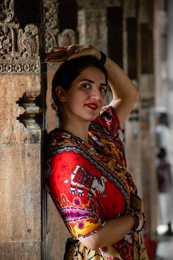 A portrait of a woman in traditional dress leaning against a wooden pillar in a temple in Sri Lanka