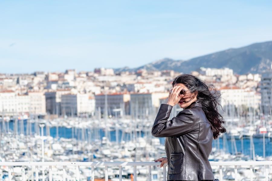 A woman by the port of Marseille trying to hold her hair with her hands against the strong wind