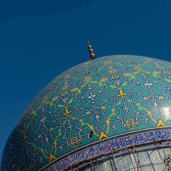 One of the majestic domes of Shah Mosque, adorned with intricate golden and turquoise tilework. Islamic inscriptions embellish the dome, showcasing the genius of Persian architectural design