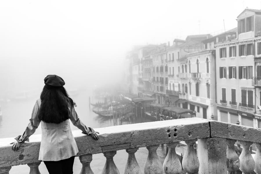 Portrait of a woman standing on the Rialto Bridge in Venice, looking out over a misty canal