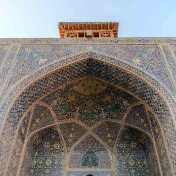 One of the main mihrabs at Imam Khomeini Mosque, framed by an antique wooden clock. Golden tiles shimmer in the sunset light, emphasizing authentic Persian tilework and architectural elegance